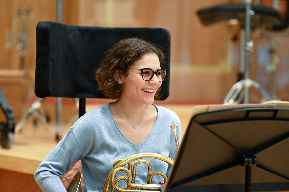 A student holding a french horn and laughing in rehearsal in the Amaryllis Fleming Concert Hall